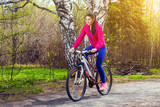 Young woman rides a bike along a path in the forest at sunset of a summer day