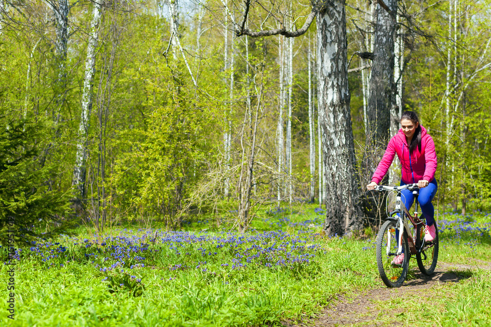 Beautiful athletic woman walking in a spring forest on a bicycle