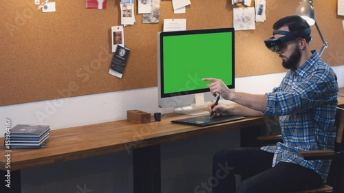 Young adult Caucasian male using holographic augmented reality glasses, creating a model on a computer screen. Green screen chroma key. 4K UHD RAW edited footage photo