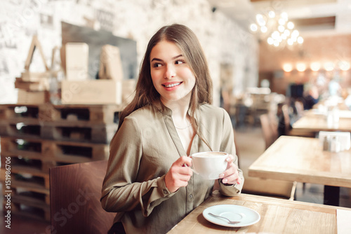 Pretty girl using cell phone smiles and looks over her shoulder out of frame.In caffe.