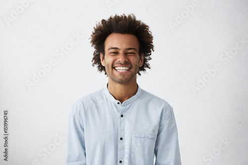 Handsome unshaven young dark-skinned male laughing out loud at funny meme he found on internet, smiling broadly, showing his white straight teeth. Positive human facial expressions and emotions photo