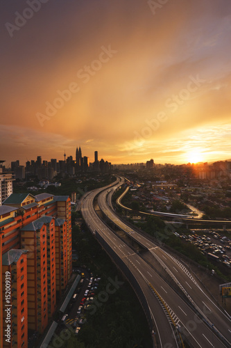 Sky and cloud turn into golden color during sunset overlooking a city where a well built highway giving a unique perspective. Capture in portrait format. © nazmanm