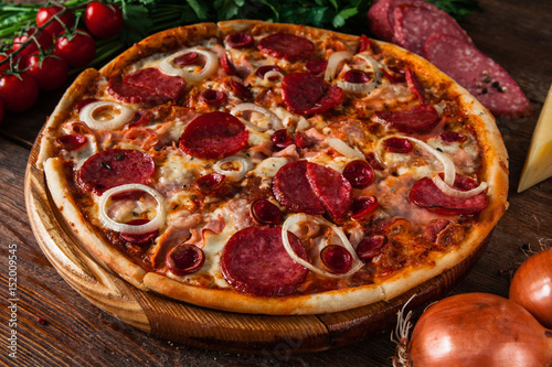 Fresh italian pizza with sausage assortment, ham, cheese and onion, on wooden background with ingredients. Restaurant menu photo.