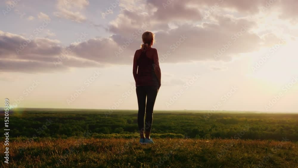 Silhouette of a woman standing on a hill top facing the sun. Against a background of a very beautiful valley. Back view. Concept - man and nature, active and healthy way of life, faith and religion Silhouette of a woman standing on a hill top facing the sun. Against a background of a very beautiful valley. Back view. Concept - man and nature, active and healthy way of life, faith and religion