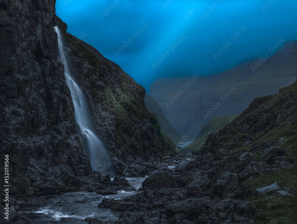 Lightbeam over waterfall in small valley at nightfall, Faroe Islands.