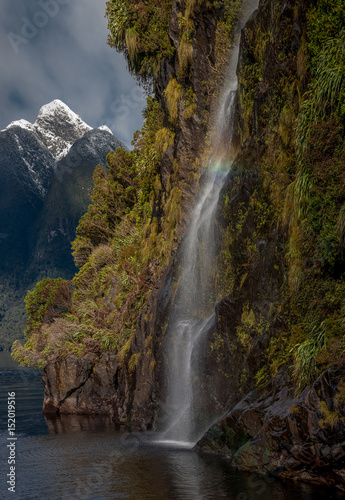 Close up of waterfall falling over a cliff into the sea with snow-capped mountains in the background  Doubtful Sound  New Zealand.