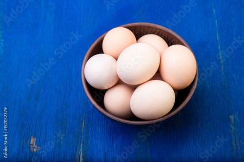 Fresh eggs in a brown bowl on blue background. Top view