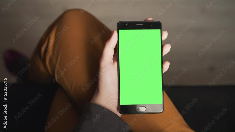 Handheld shot of female teen hands using smartphone with green screen sitting near window, uhd prores footage