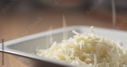 grated pizza mozzarella cheese falls in plate, 4k photo