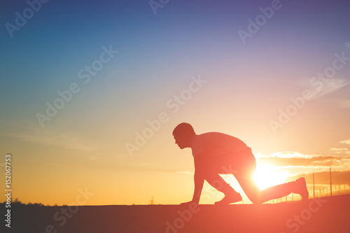 Silhouette of man in position to run on sunset background
