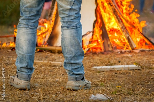 Man in blue jeans looking at the burning bonfire stock image.