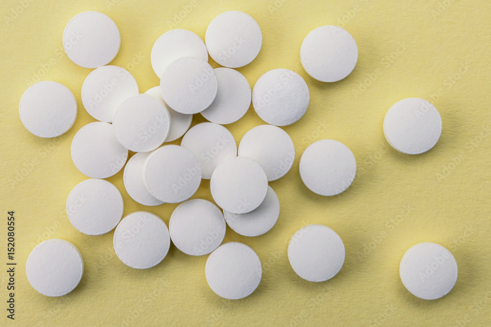 Many medicines white pills capsules on yellow bacground