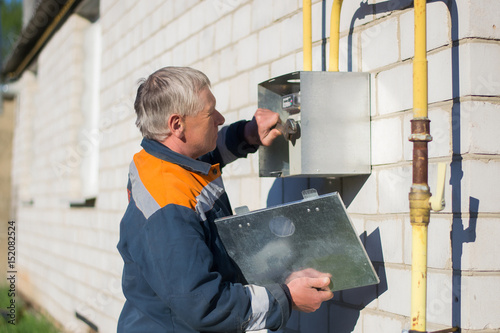 A gray-haired master specialist man repairs a gas meter hanging on a brick wall. Maintenance of gas equipment photo