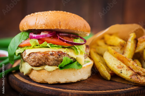 Big sandwich - hamburger with juicy beef burger, cheese, tomato, and red onion on wooden background