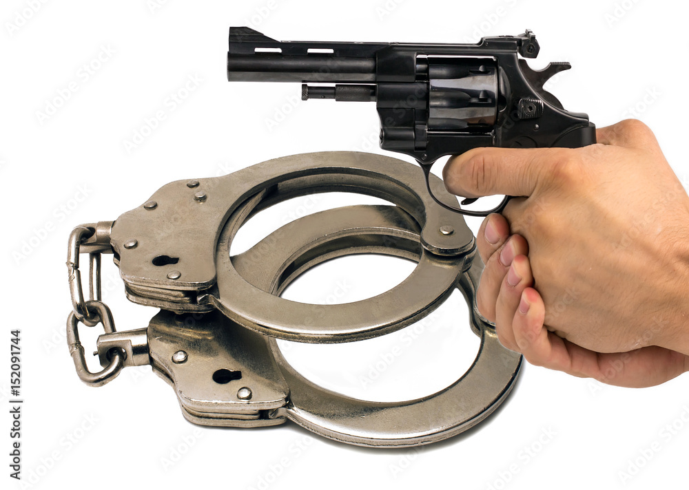 Obraz premium Gun in hand against the background of police handcuffs.justice.
