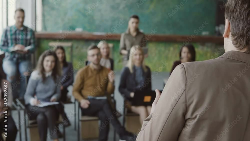 Young businessman standing in front of group of young people and talking. Business conference at modern office, seminar. Young businessman standing in front of group of young people and talking. Business conference at modern office, seminar.