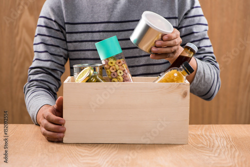 Volunteer with donation box with foodstuffs on wooden background © makistock