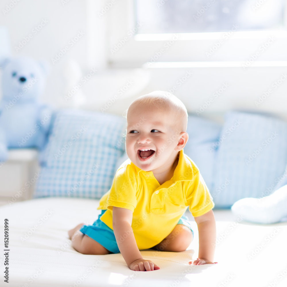 Baby boy playing on bed in sunny nursery Baby boy playing on bed in sunny nursery
