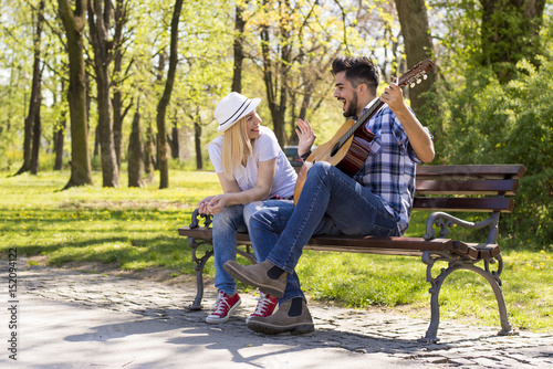 Couple sitting on the park bench playing guitar on beautiful sunny day
