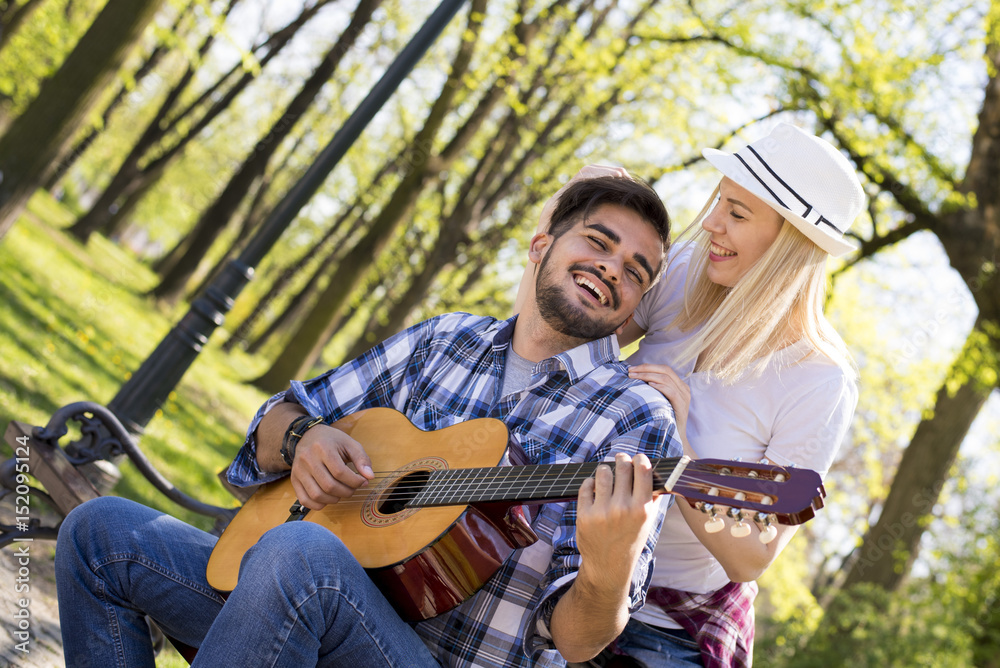Couple sitting on bench and playing guitar on beautiful sunny day