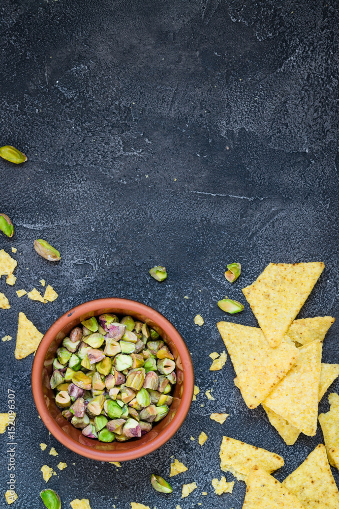 Chopped pistachios in a bowl with chips on dark background. Top view with copy space Chopped pistachios in a bowl with chips on dark background. Top view with copy space