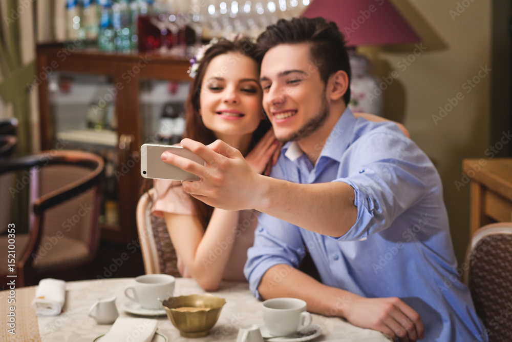 Young enamored couple sitting at a table in a cafe and making selfie Young enamored couple sitting at a table in a cafe and making selfie