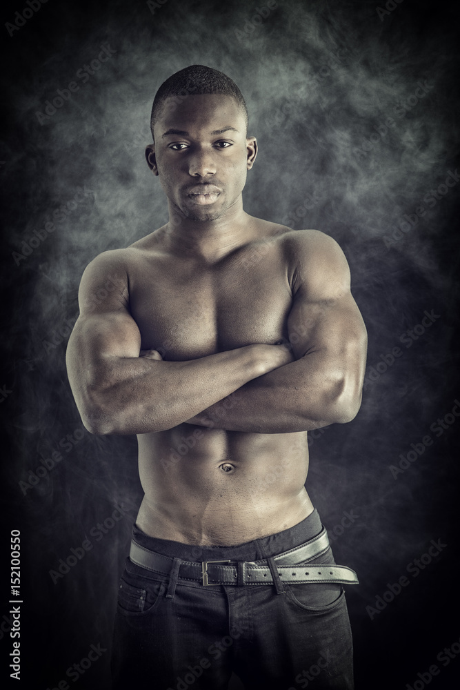 Handsome shirtless muscular black young man, looking at camera, on dark background in studio shot