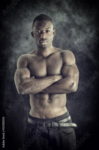 Handsome shirtless muscular black young man, looking at camera, on dark background in studio shot