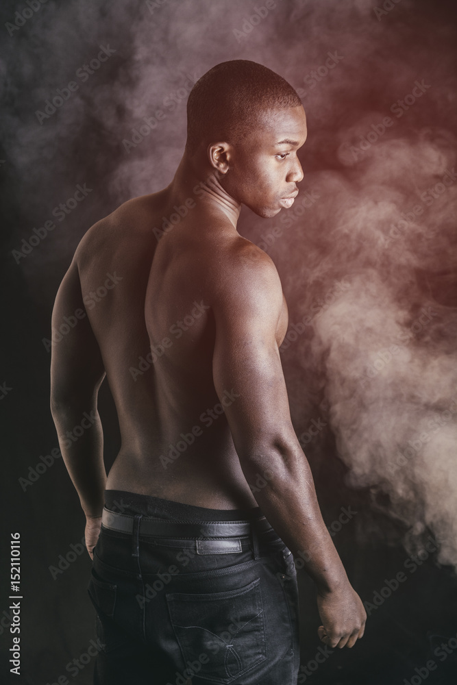 Handsome shirtless muscular black young man, looking at camera, on dark background in studio shot