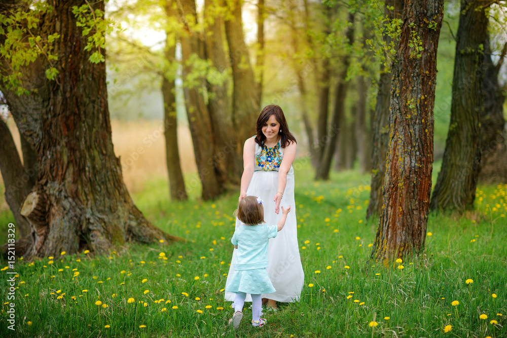 pregnant mother walks in the park with the daughter on a sunset, play and have fun
