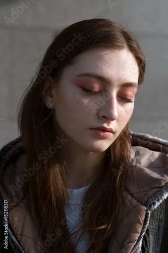 A beautiful and fashionable girl in a fur coat walks in the city on a sunny day