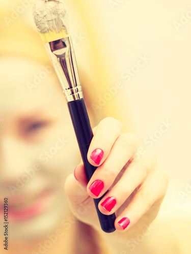 Woman applying with brush clay mud mask to her face