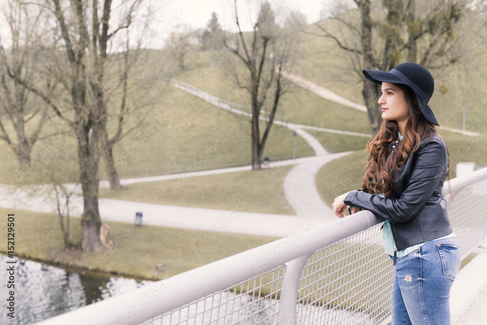 Portrait of young woman standing on a bridge, she is wearing a black hat.