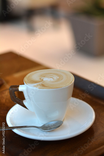 Cup of foamy cappuccino on a plate on a wooden table.