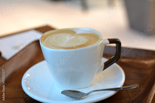 Cup of foamy cappuccino on a plate on a wooden table.