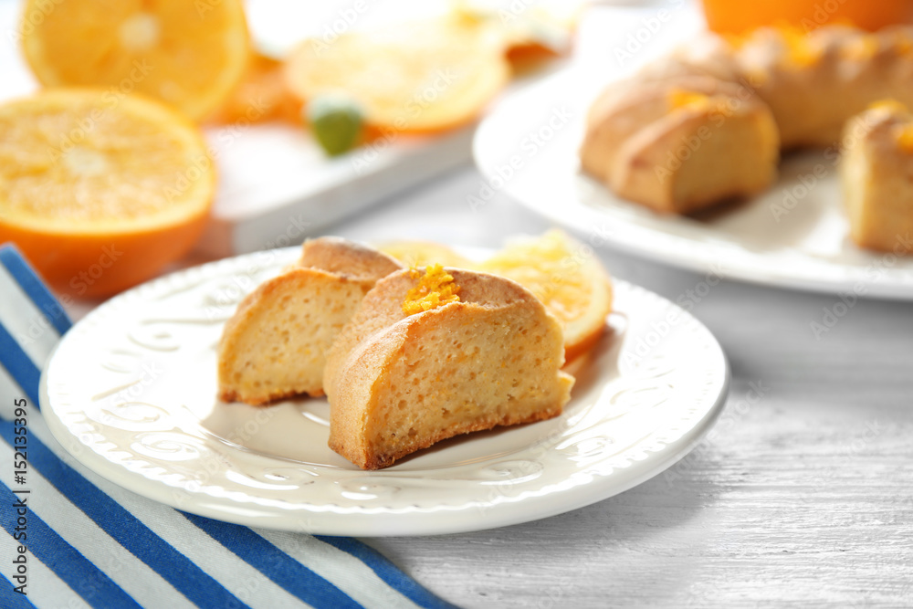 Plate with slices of citrus cake and fresh orange on white wooden table