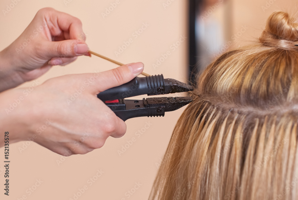 Naklejka premium The hairdresser does hair extensions to a young girl, a blonde in a beauty salon. Professional hair care.