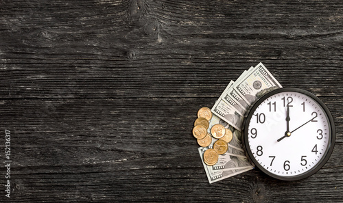 Clock with money on black wooden background. Time is money.