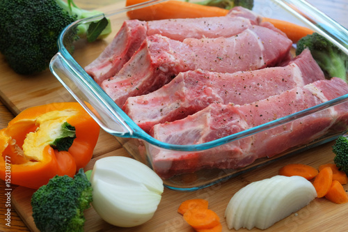 Country style raw pork ribs with vegetables in glass hit-resistant dish prepared for roasting in oven