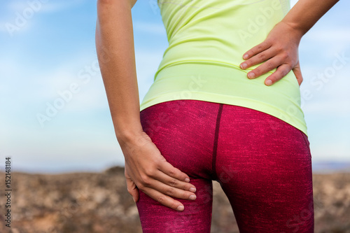 Lower back glute muscle pain cramp athlete runner. Running woman athlete on outdoor trail run holding leg with painful behind injury, strained legs, hurting butt or sore body.