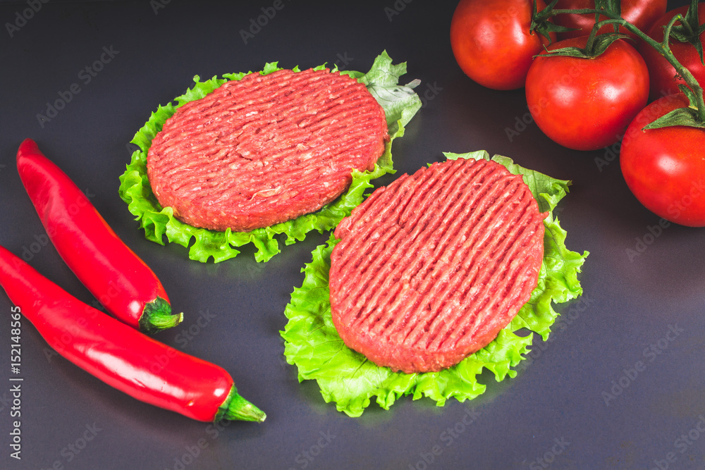 Raw burgers with lettuce on a gray background. Tomatoes, peppers Raw burgers with lettuce on a gray background. Tomatoes, peppers