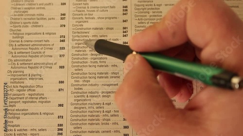 Businessman is reading, marking and making notes in the phonebook