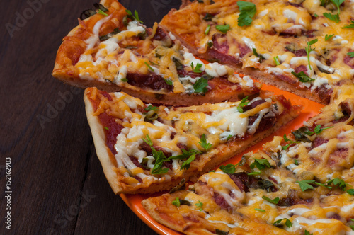 Pizza and two cut pieces on a dark wood background