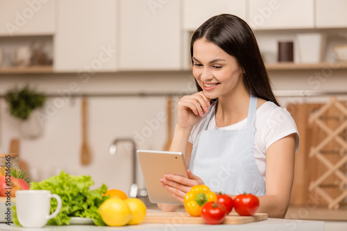 Young Woman in kitchen with the tablet computer looking recipes, smiling. Food blogger concept