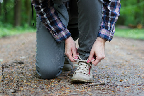 A hiking woman binds tourist walking shoes on a forest path. 