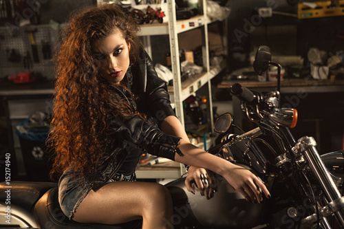 Beautiful young biker woman on her motorcycle at the workshop