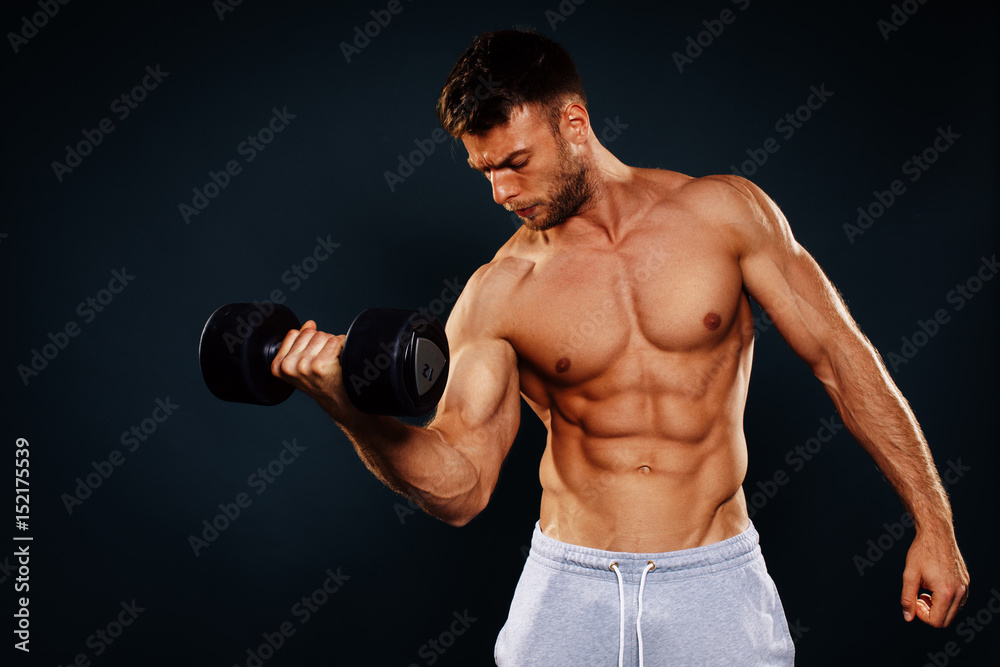 Attractive fitness man holding dumbbells in the hands in studio