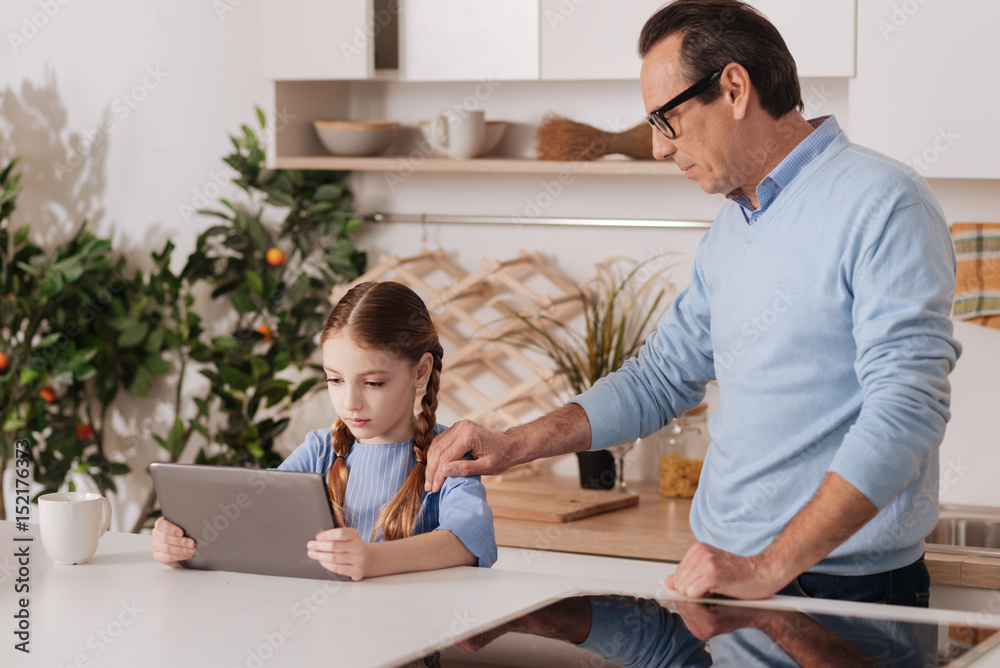 Obraz premium Serious grandfather asking granddaughter stop playing with gadget indoors