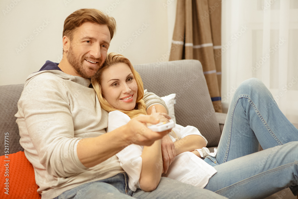 Happy mature couple using remote control while resting at home Happy mature couple using remote control while resting at home