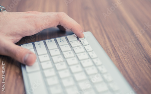 Man's hand pressing escape button on wireless keyboard on wooden table. Key combination.